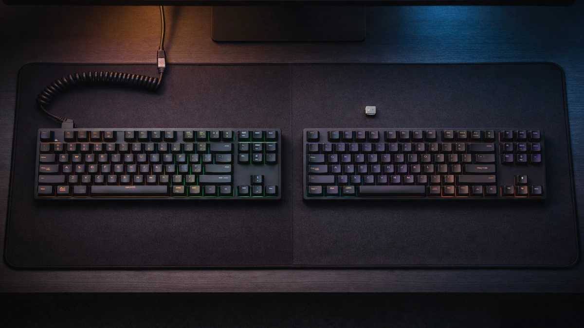 Două tastaturi de gaming pe birou, una cu fir și una wireless, ilustrând diferențele de conectivitate