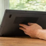 Mână care atinge orificiile de ventilație de pe partea de jos a unui laptop fierbinte