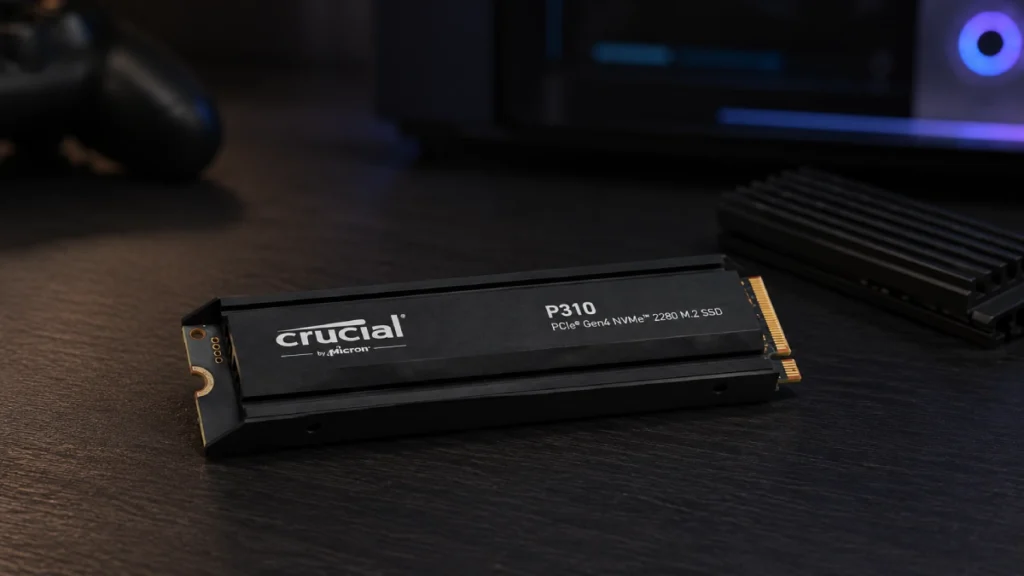 SSD Crucial P310 2TB fără heatsink, așezat pe o masă lângă un radiator M.2 separat, pregătit pentru montaj pe PlayStation 5
