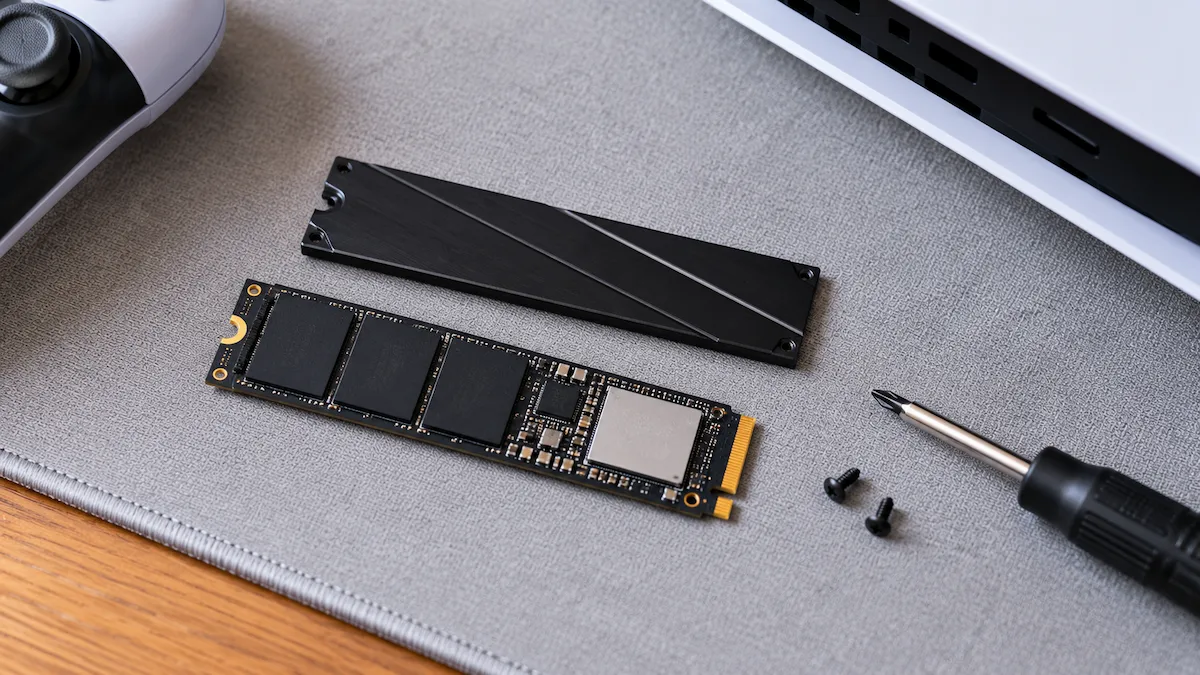 SSD M.2 și radiatorul lui subțire de aluminiu pe un mousepad gri, lângă o șurubelniță și două șuruburi