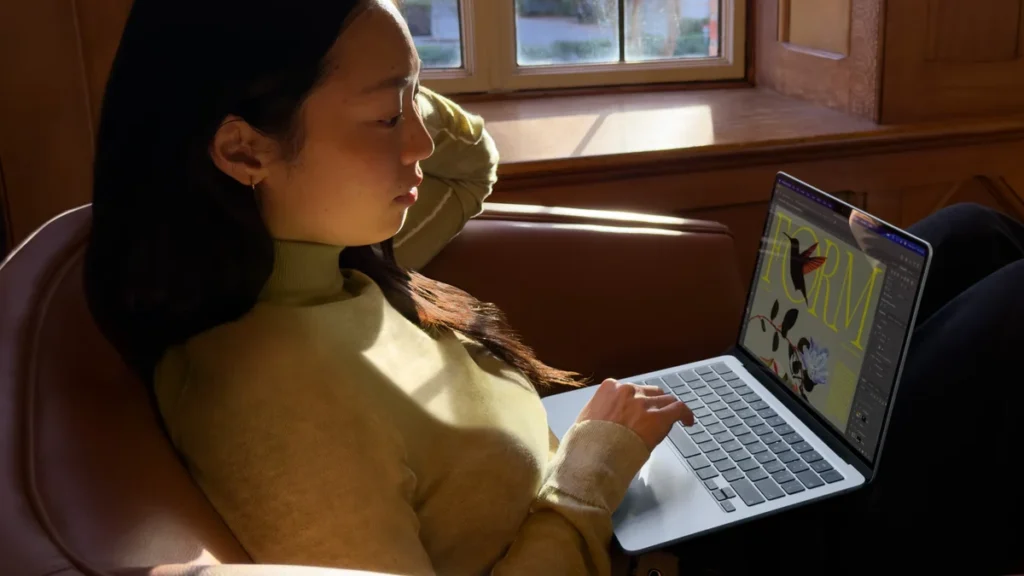 O persoană lucrează pe un Apple MacBook Air 13 M5 ținut pe genunchi, într-un fotoliu de lângă fereastră