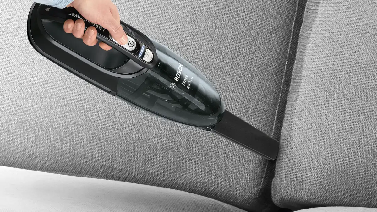 Aspiratorul de mână Bosch BHN24L negru, folosit pe o canapea gri