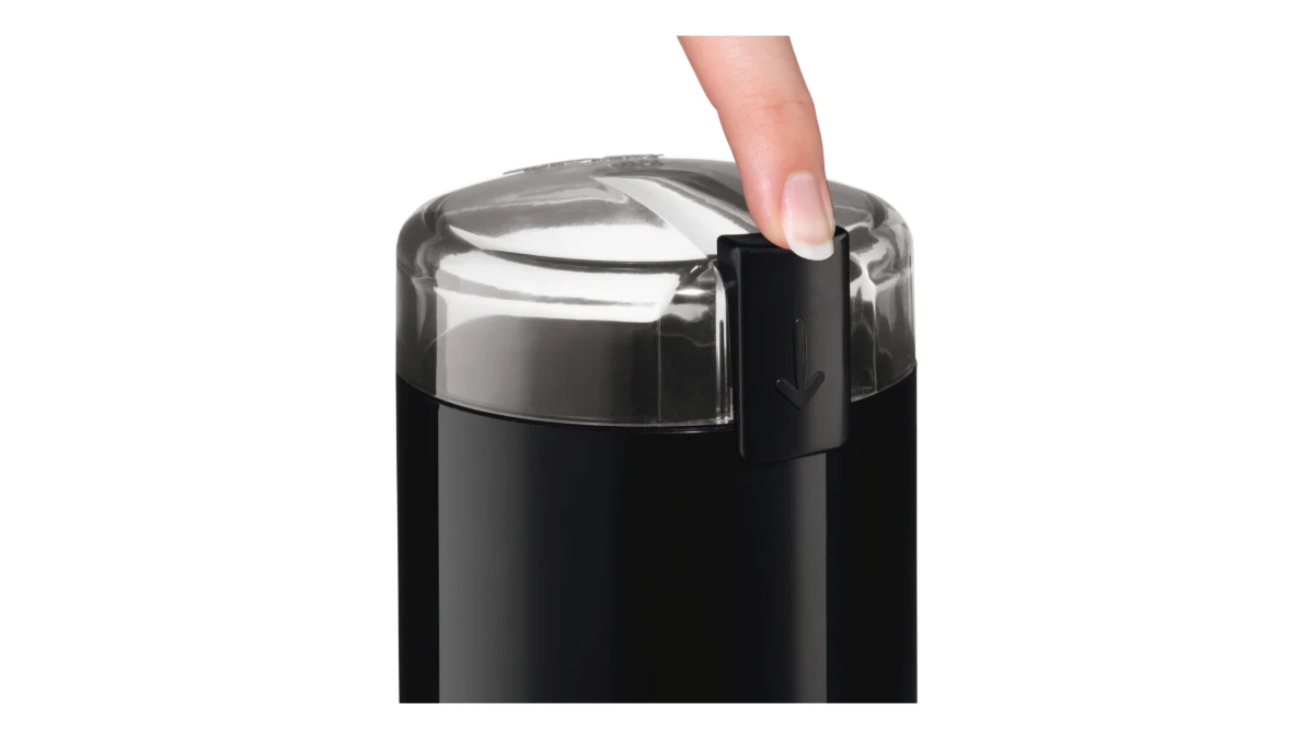 Un deget apasă butonul de pe capacul transparent al râșniței de cafea Bosch TSM6A013B, neagră