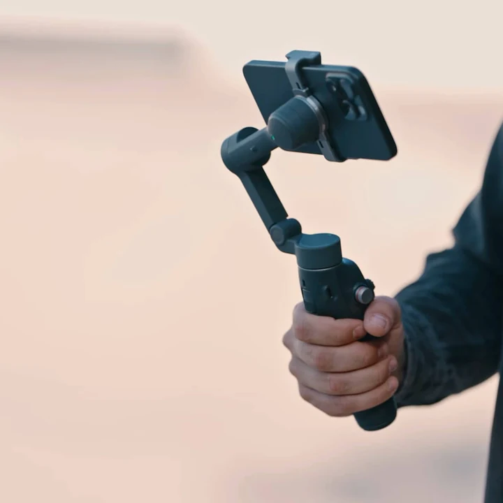 Mână care ține gimbalul DJI Osmo Mobile 8 cu un telefon în clemă
