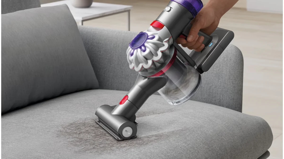 Aspiratorul de mână Dyson V8 Car+Boat cu mini peria motorizată, pe o canapea gri