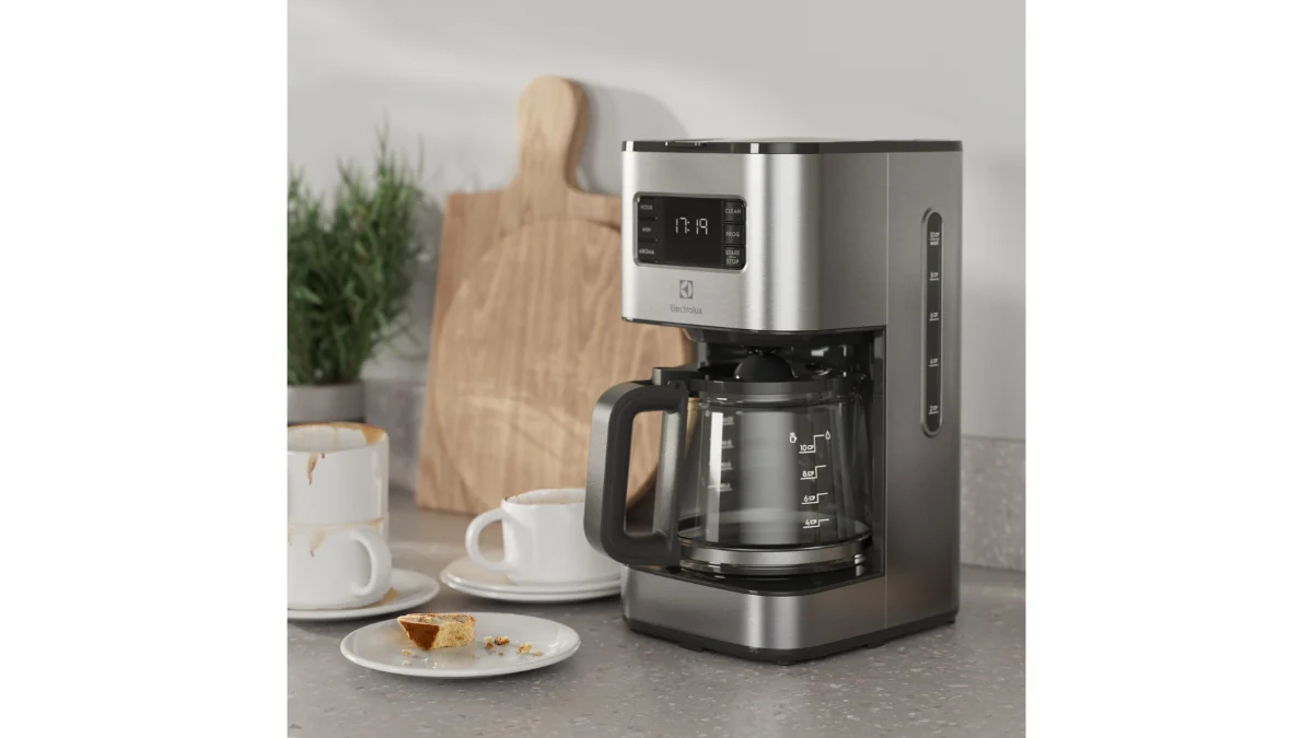 Cafetiera Electrolux Create 5 E5CM1-6ST din inox, cu carafa de sticlă plină, pe un blat de bucătărie lângă o ceașcă de cafea