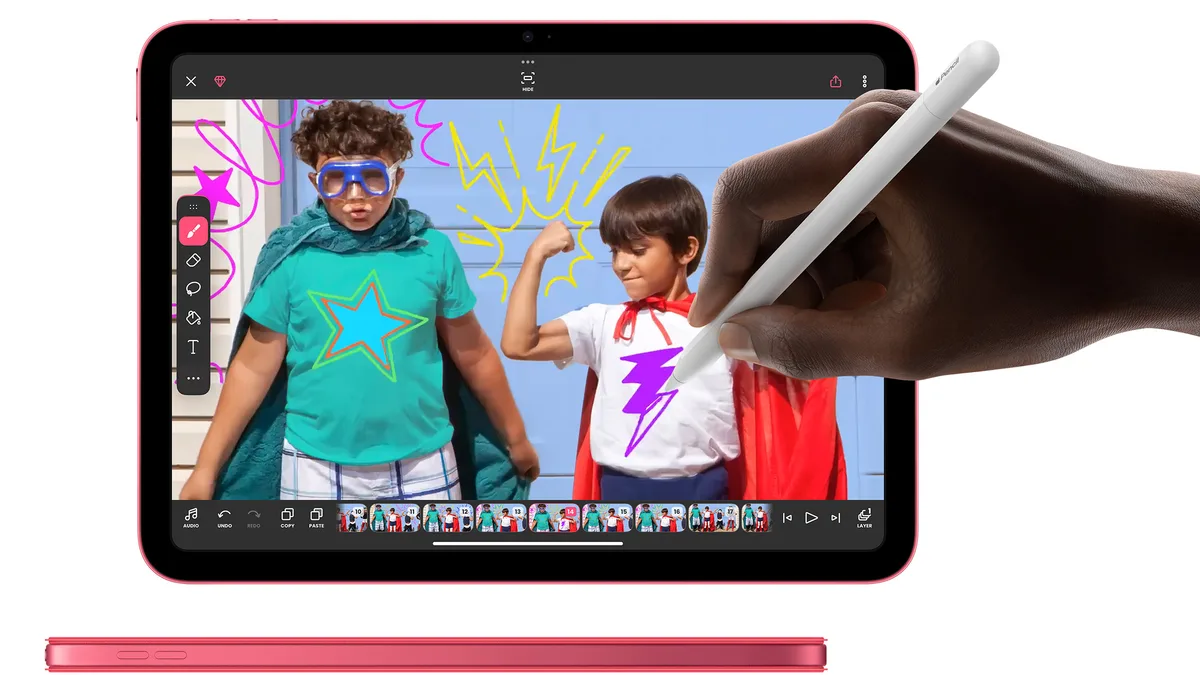 Mână care desenează cu Apple Pencil pe un iPad 11 roz, peste o fotografie cu doi copii costumați în supereroi