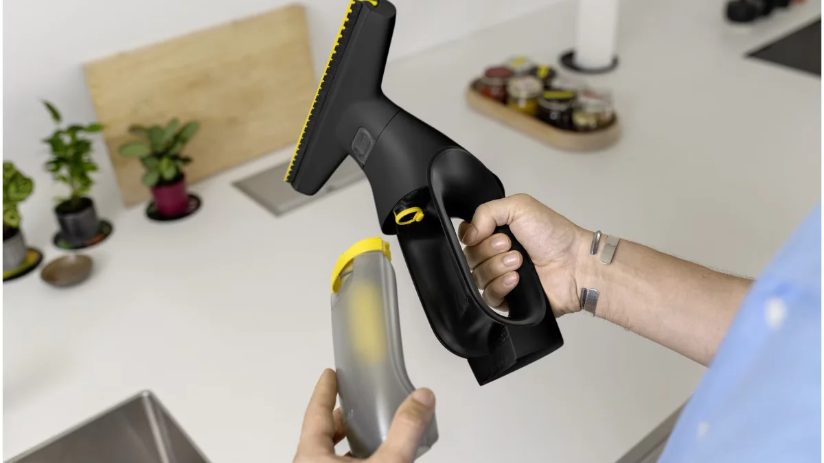 Aspiratorul de geamuri Kärcher WV 2 Universal Precision+ Black, negru cu galben, ținut în mână deasupra unei chiuvete în timp ce i se golește rezervorul de apă murdară