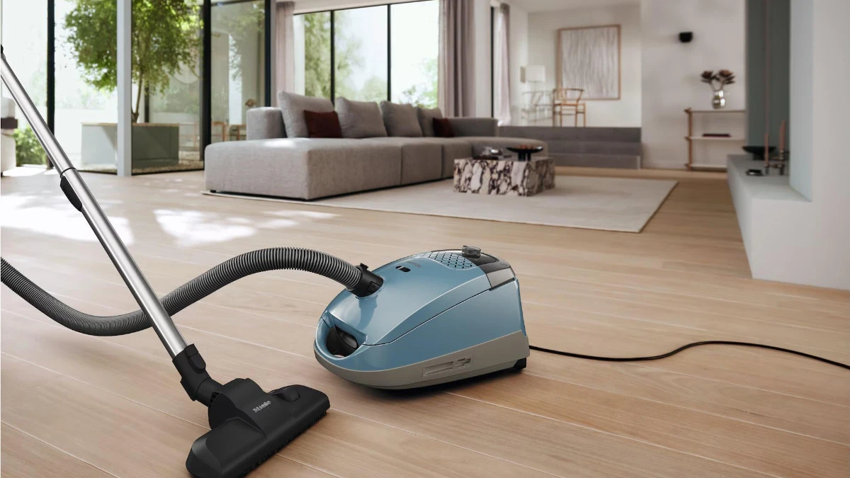 Aspirator cu sac Miele Guard S1 albastru, folosit pe un parchet de lemn într-o cameră de zi luminoasă