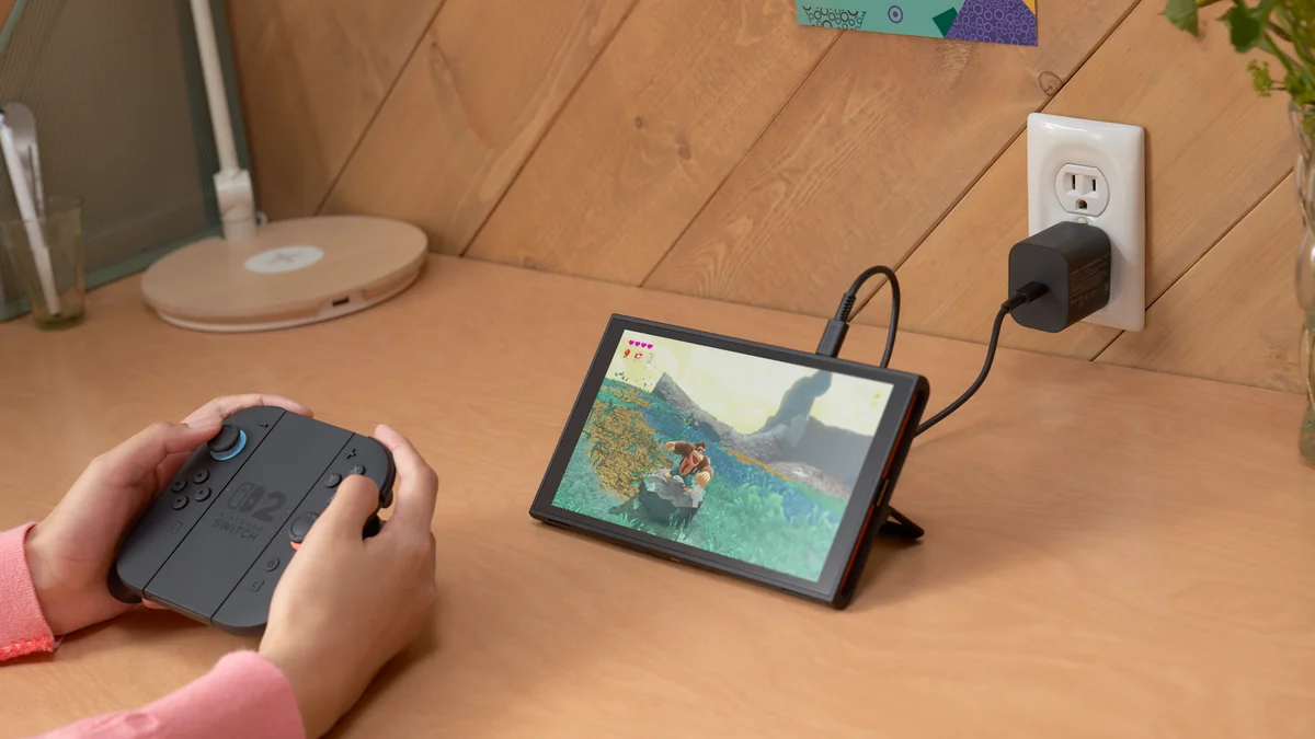 Nintendo Switch 2 pe suportul din spate, la încărcat, iar un jucător ține Joy-Con 2 atașate pe grip