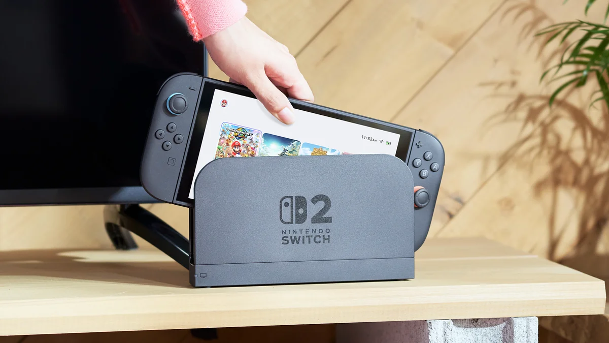 Nintendo Switch 2 introdusă în dock, lângă un televizor, pe un raft de lemn