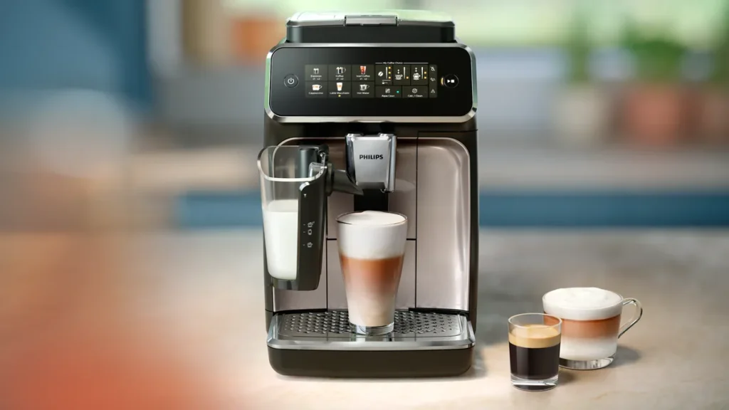 Espressor automat Philips seria 3300 cu recipientul de lapte LatteGo, un latte macchiato sub duză și două cești de cafea pe blatul bucătăriei