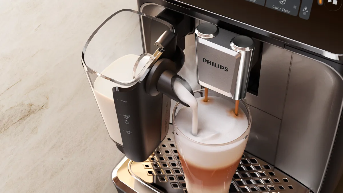 Recipientul LatteGo al espressorului Philips seria 3300 turnând spumă de lapte într-un pahar de latte macchiato, lângă duzele de cafea