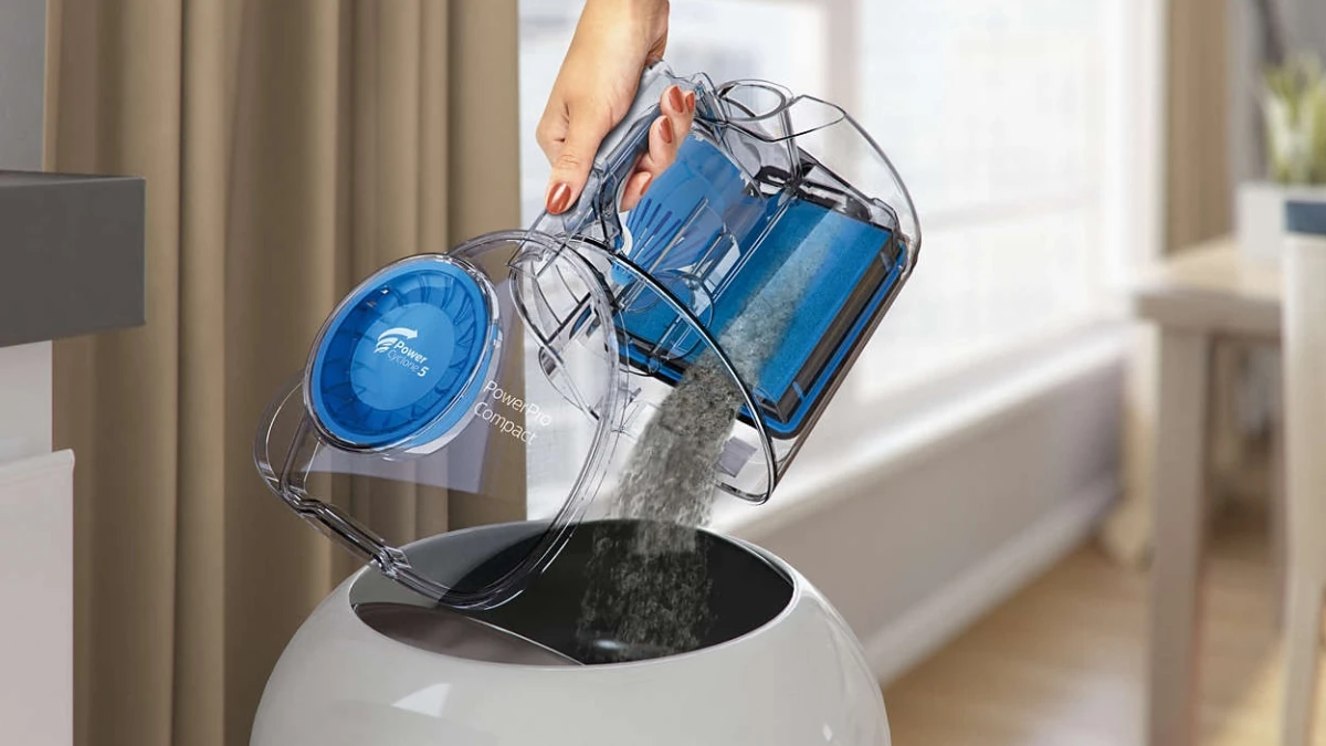 Recipientul de praf albastru al aspiratorului Philips PowerPro Compact FC9334/09, golit cu o singură mână într-un coș de gunoi