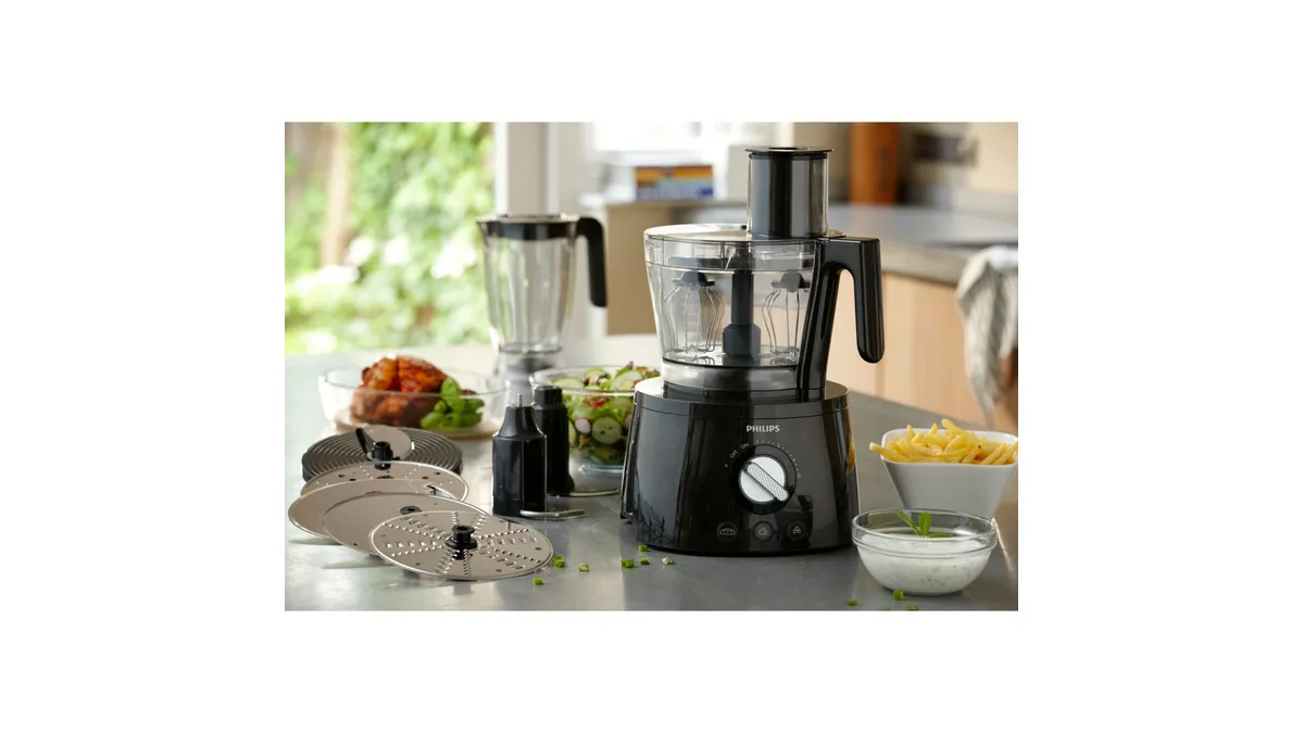 Robotul de bucătărie Philips Seria 7000 HR7776/90, negru, cu bolul și blenderul pe un blat de bucătărie, lângă legume