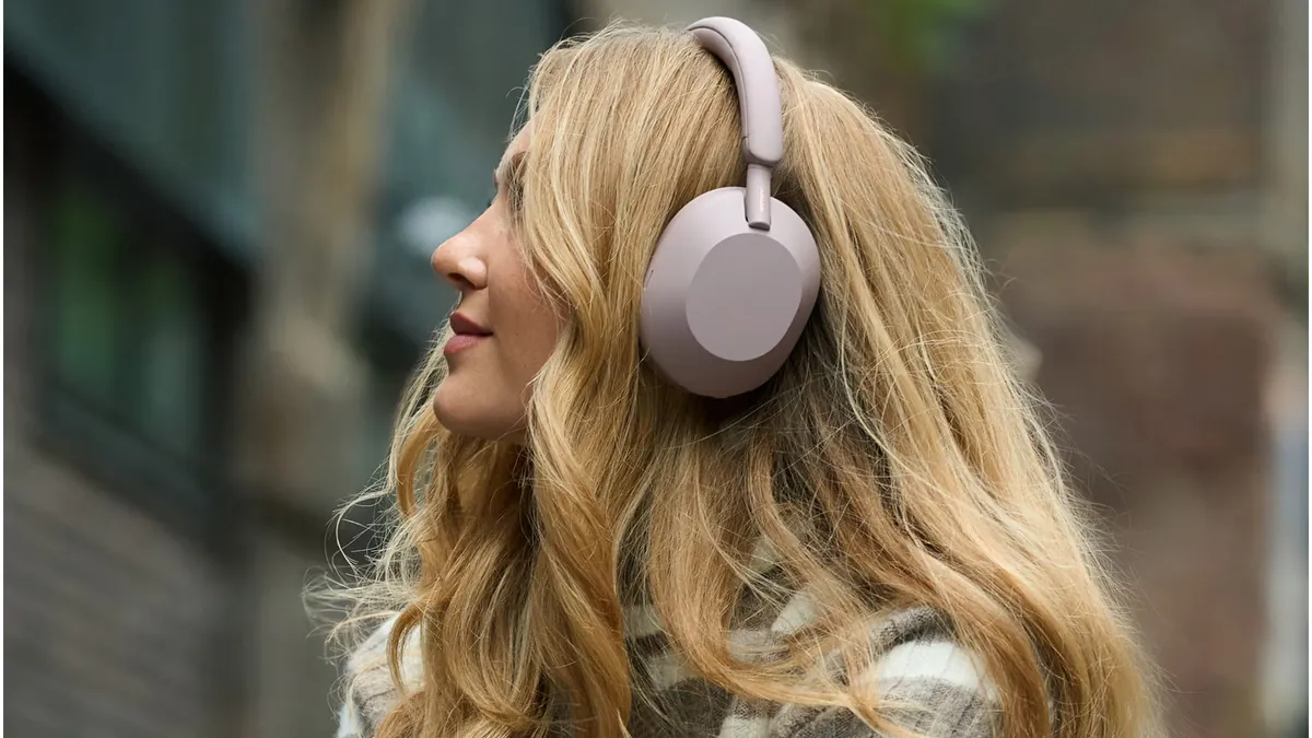 Femeie în profil, pe stradă, cu căștile Sony WH-1000XM5 în nuanță roz pal pe cap