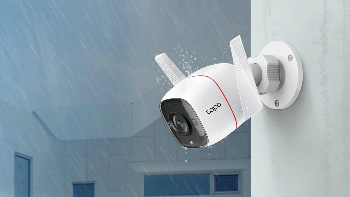Camera Tapo C310 prinsă cu suportul pe colțul unei case, sub ploaie, cu picături pe carcasă și antene