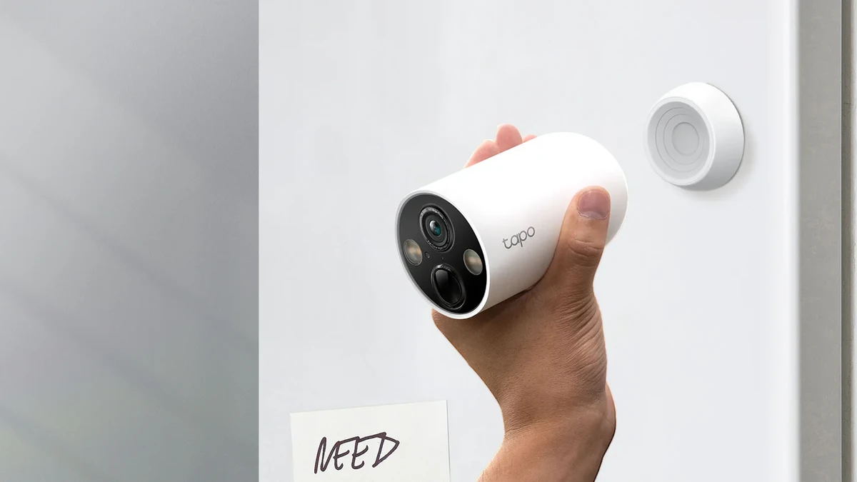 Mână care ține camera Tapo C425 lângă baza magnetică fixată pe o ușă albă