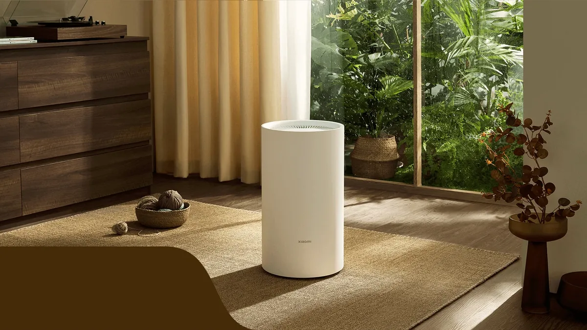 Dezumidificatorul Xiaomi Smart Dehumidifier Lite pe un covor din sufragerie, lângă o comodă de lemn și o fereastră mare spre grădină